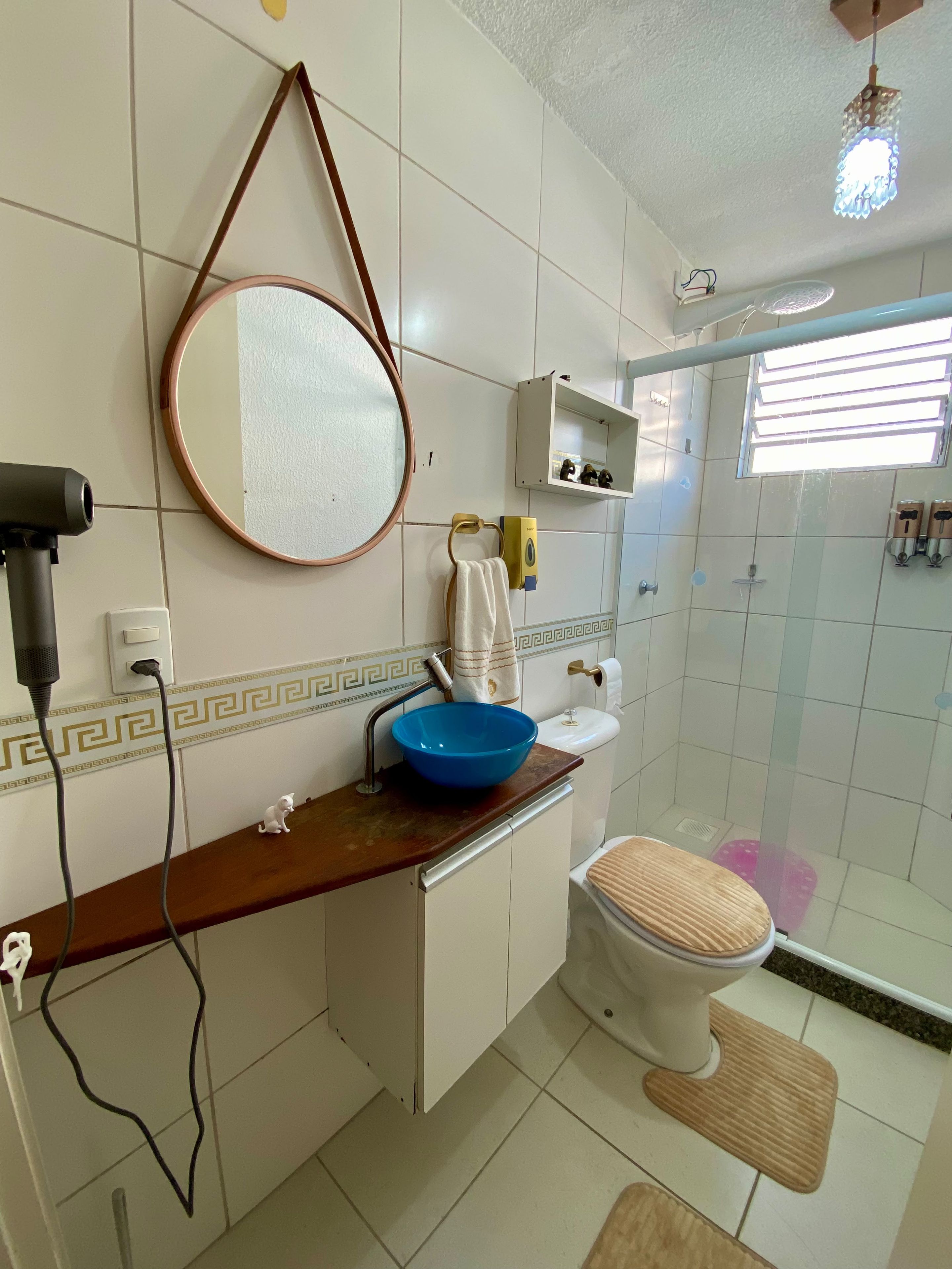 Un bagno con il water, un lavabo con una bacinella blu, uno specchio, un portascopevoli, una zona doccia e un piccolo ripiano con articoli da toilette.