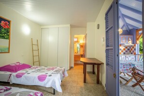 A room with two beds, a table, and a door leading to a balcony. - New Listing (Saint-Pierre)