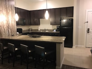 A kitchen with dark cabinets, a black refrigerator, a granite countertop, and bar stools. - CANYON VILLAGE/CLUB WYNDHAM PARK CITY, 3BR, FEB 6-9,2027, GREATEST SNOW ON EARTH (Park City)