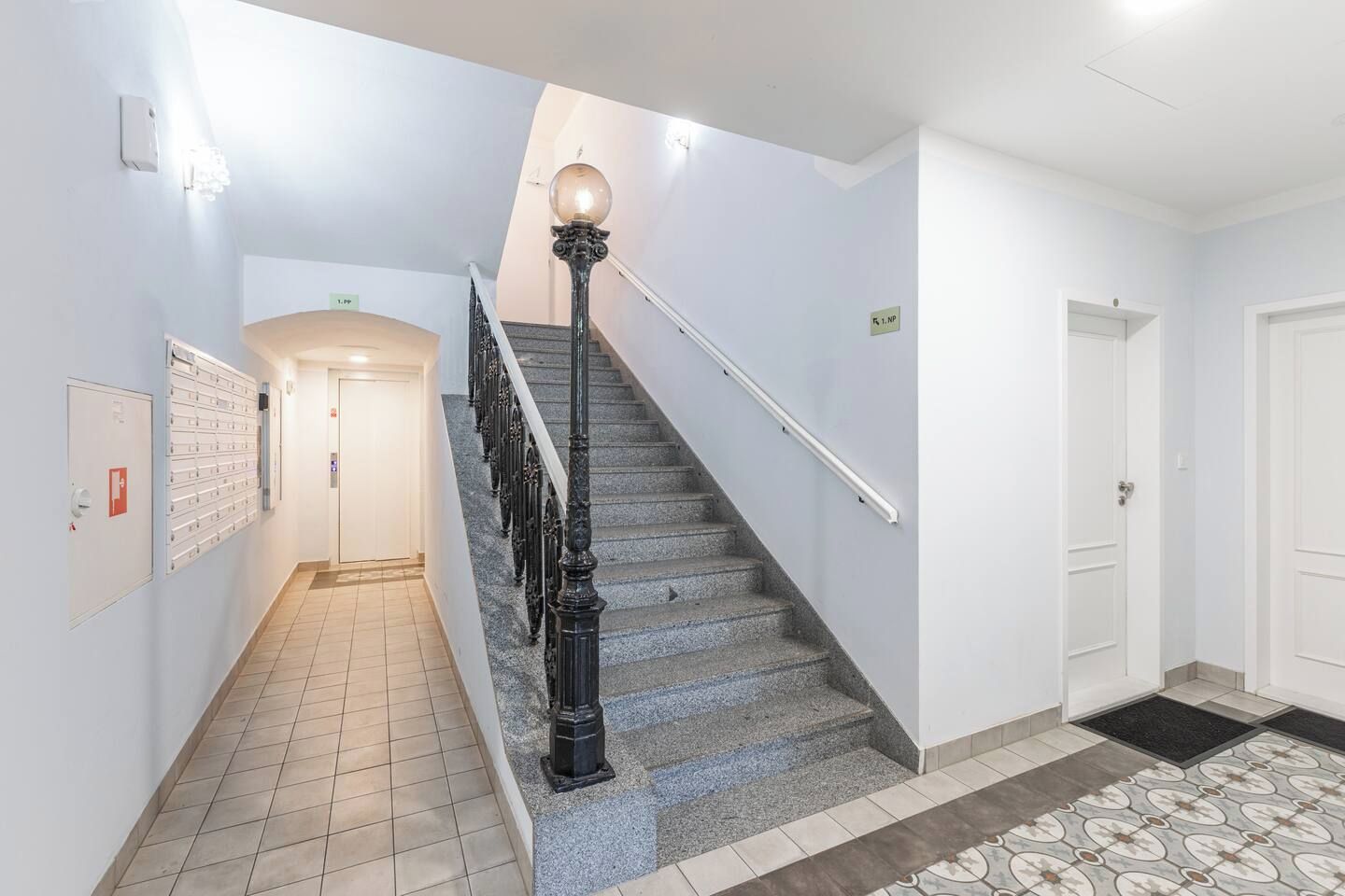 A staircase with a handrail, a light fixture at the top, and a tiled floor.