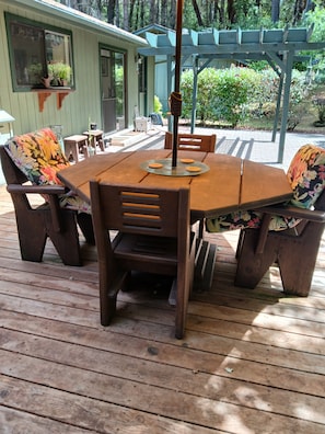 Eine Holzterrasse mit Tisch und Stühlen, einer Pergola und einem Haus im Hintergrund.