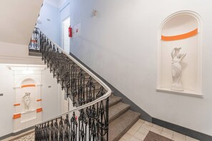 A staircase with ornate black railings, a white statue on the wall, and a fire extinguisher mounted on the wall. - Nově zrekonstruovaný byt vedle Národního muzea (Praha 1)