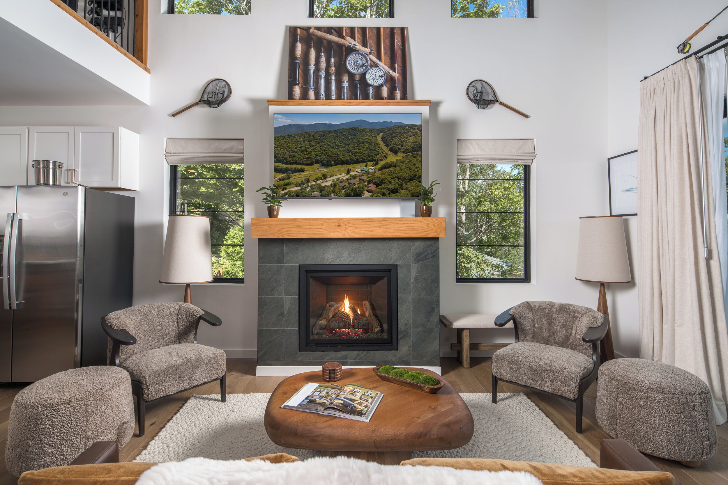 A modern living room with a fireplace, two armchairs, a coffee table, and a large window with a scenic view.