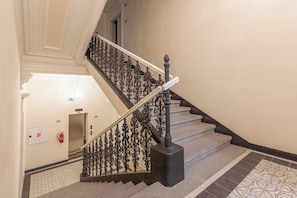 Eine Treppe mit aufwendig gestalteten, schwarzen Geländern und einer weißen Handlauf, die zu einem Aufzug führt.