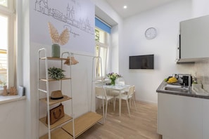 Eine moderne Küche mit Flachbildfernseher, einem Essbereich mit Tisch und Stühlen sowie einer Wanddekoration mit Stadtansicht und Blättern.