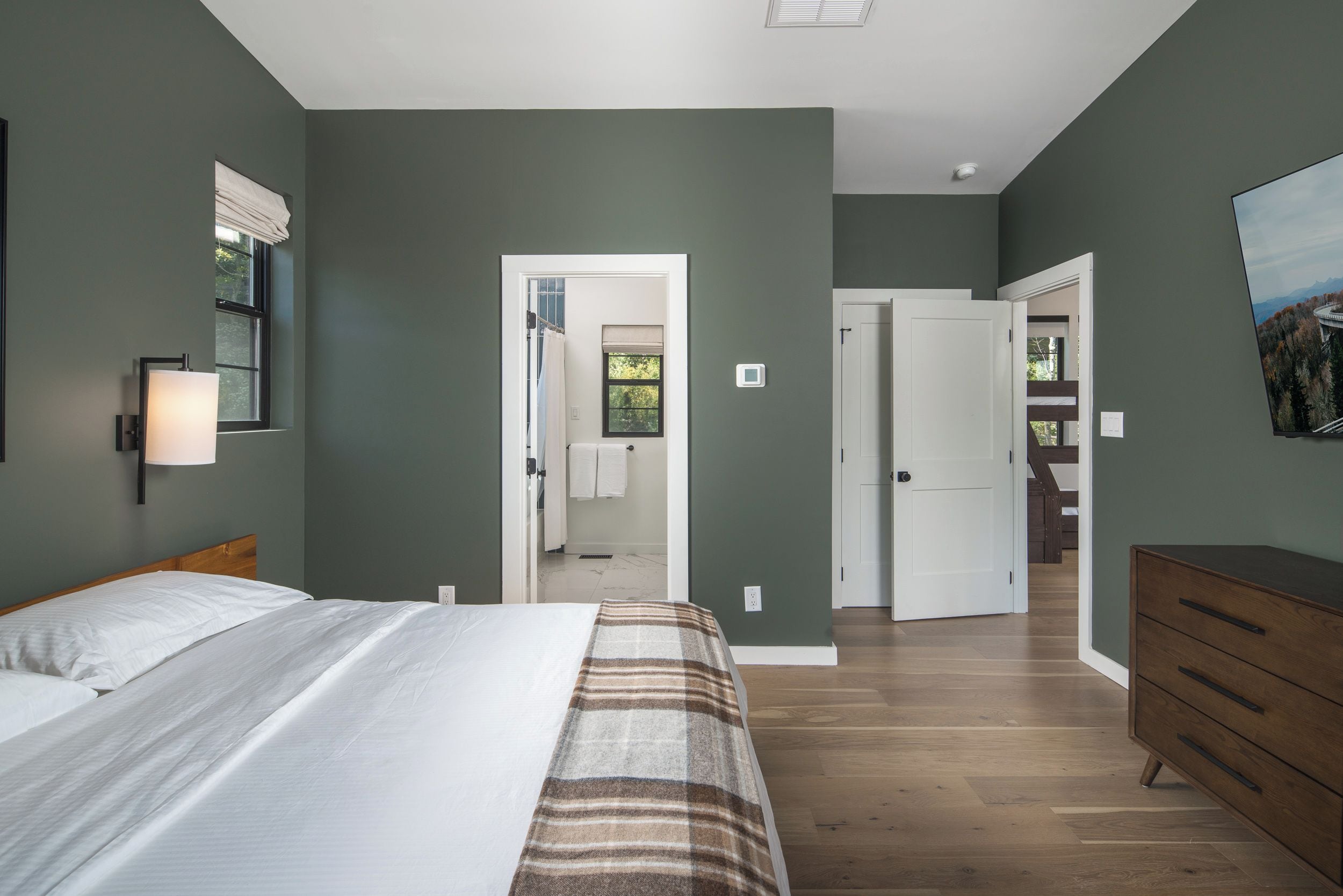 A bedroom with a bed, a dresser, and a view of a mountain landscape through an open door.