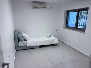 Ein kleines Zimmer mit einem Einzelbett, einem Fenster, weißen Wänden und einem Fliesenboden.