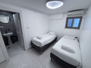 Ein kleines, sauberes Zimmer mit zwei Betten, einem Fenster, einem Waschbecken und einem Spiegel.