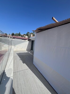 Eine Dachterrasse mit blauem Himmel, einer weißen Wand und einem Fliesenboden.