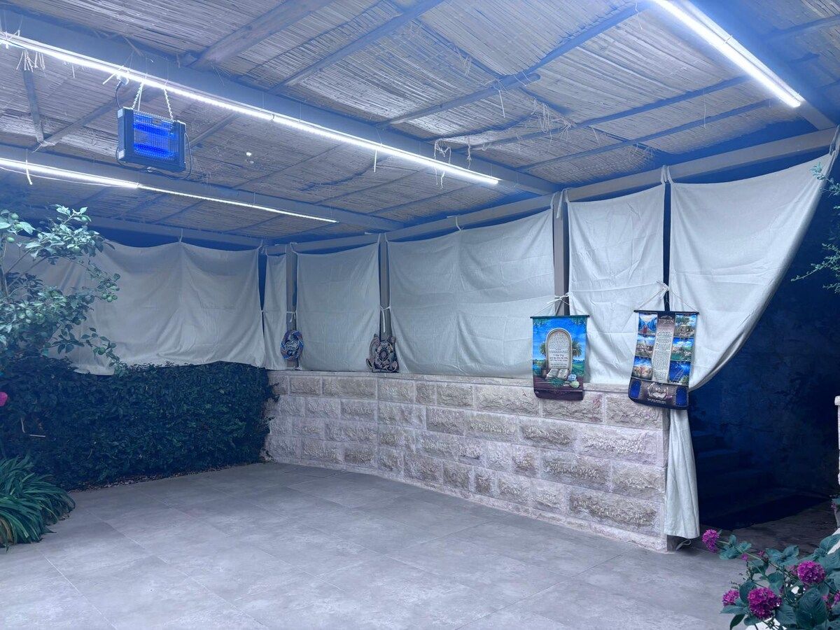 Un espace extérieur abrité, doté d’un mur en pierre, de décorations suspendues et d’un écran bleu.