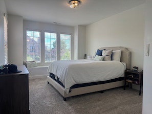 A bedroom with a bed, bedside table, lamp, and a view of the outside through large windows. - Charming House in Little Valley (St. George)