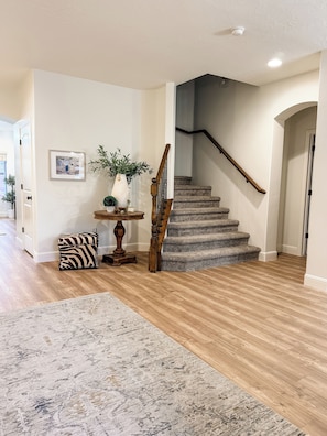 A staircase with a wooden handrail and carpeted steps, a small table with a vase and picture frame, and a zebra-patterned ottoman. - Charming House in Little Valley (St. George)
