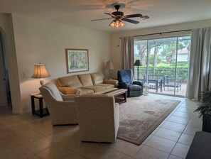 A living room with a sofa, two armchairs, a coffee table, a ceiling fan, and a large sliding glass door leading to an outdoor area. - Pelican Preserve-Fort Myers - Top 55 + active --2 bdrm 2 bath Villa turn key (Fort Myers)