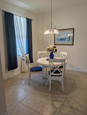 A dining area with a round table, white chairs, a blue vase with flowers, and a chandelier. - Pelican Preserve-Fort Myers - Top 55 + active --2 bdrm 2 bath Villa turn key (Fort Myers)