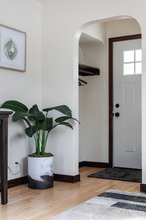 Un couloir avec une plante en pot, une œuvre d’art encadrée et une porte.