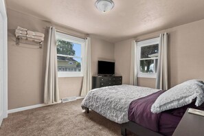 Une chambre à coucher avec un lit, une commode, un téléviseur et une fenêtre.