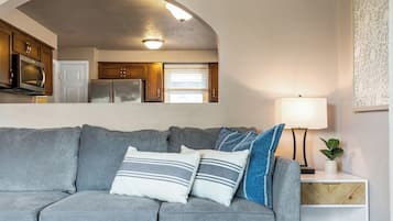 Una sala de estar con un sofá gris, una mesa de centro redonda y una mesita de noche blanca con una lámpara.