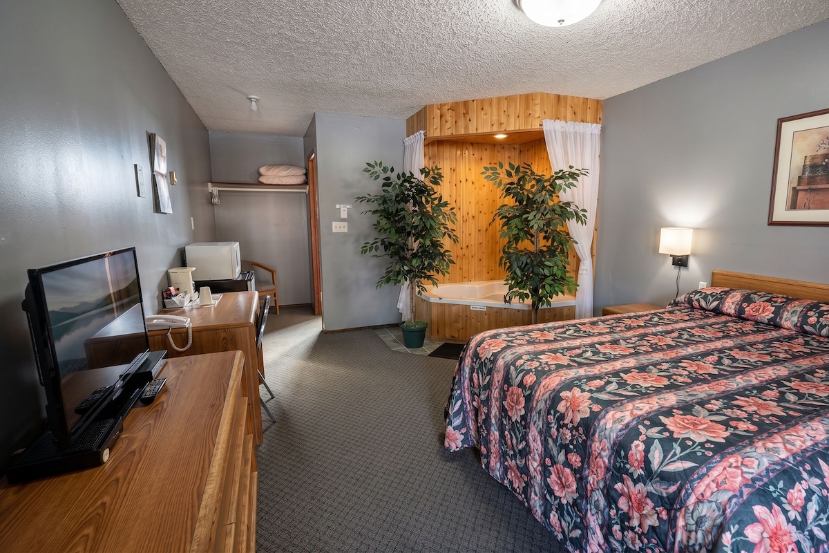 A hotel room with a bed, desk, chair, and a small bathroom area.