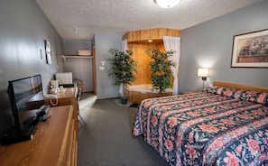 A hotel room with a bed, desk, chair, and a small bathroom area. - East Kootenay Motel (Fernie)