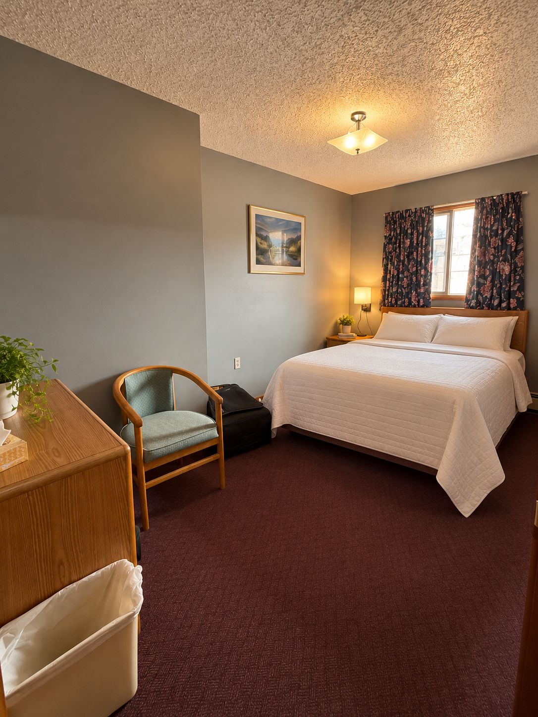 A hotel room with a bed, a chair, a desk, a lamp, and a window with curtains.