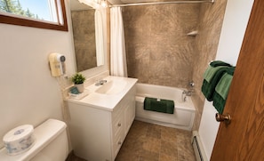 A bathroom with a white sink, a bathtub, a shower curtain, and a green towel. - East Kootenay Motel (Fernie)
