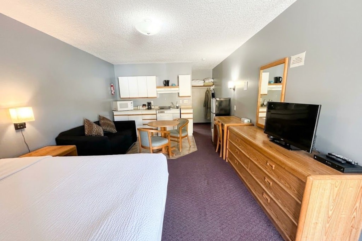 A hotel room with a bed, a desk with a television, a kitchenette, and a bathroom.