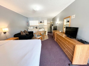 A hotel room with a bed, a desk with a television, a kitchenette, and a bathroom. - East Kootenay Motel (Fernie)
