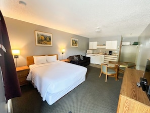 A hotel room with a bed, a desk, a chair, a sofa, and a kitchenette. - East Kootenay Motel (Fernie)