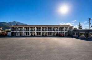 A motel with a central courtyard, a red truck parked in front, and mountains in the background.