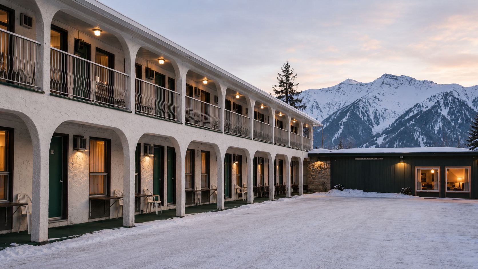 A hotel with a covered outdoor seating area, multiple balconies, and a view of snow-covered mountains.