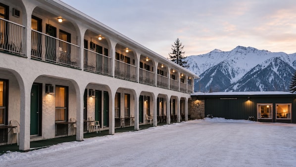 A hotel with a covered outdoor seating area, multiple balconies, and a view of snow-covered mountains. - East Kootenay Motel (Fernie)