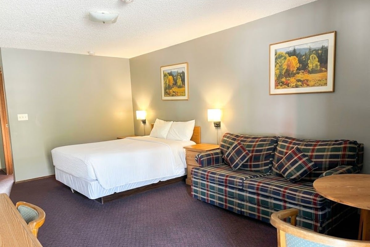 A hotel room with a bed, a sofa, a small table, and two wall-mounted lamps.