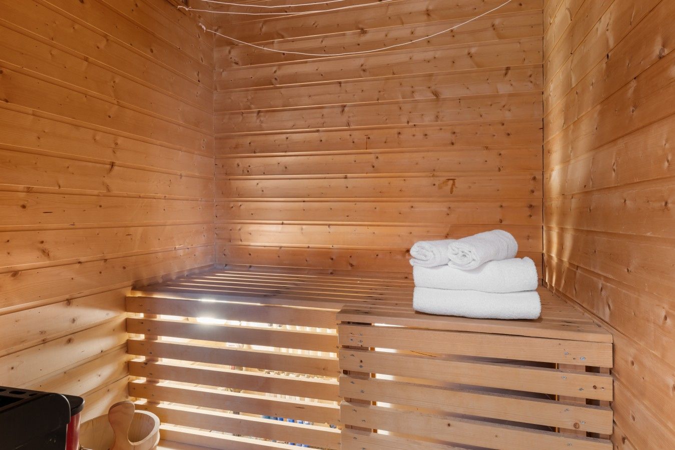 A sauna room with wooden walls and benches, a towel stack, and a sauna head.