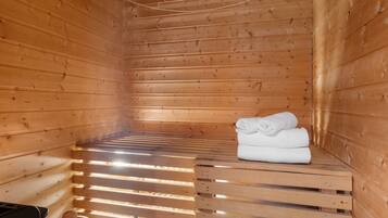 A sauna room with wooden walls and benches, a towel stack, and a sauna head.