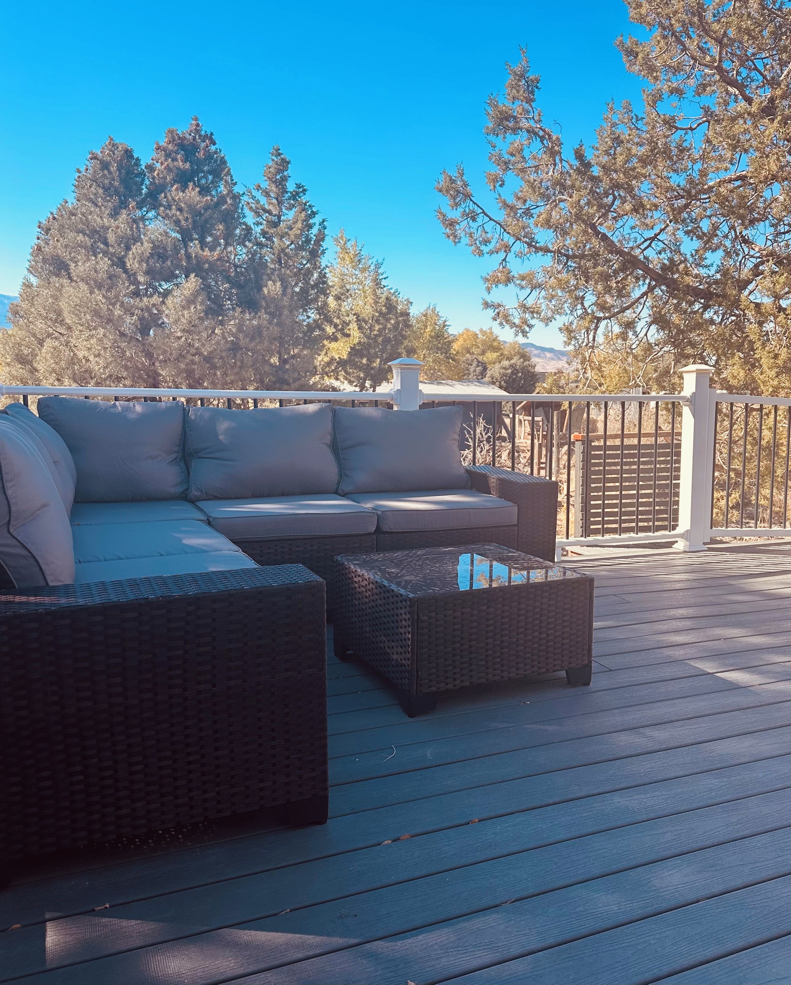 An outdoor deck with a sectional sofa, two side tables, and a pergola.