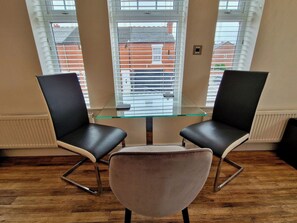 A room with a glass-top table, two black chairs with metal legs, and a single cushioned chair. - Spacious, Spacious & Modern Apt w/ Free Parking (Coventry)