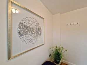 A framed artwork with a circular pattern on a wall, a plant with white flowers, and a coat rack with hooks. - Spacious, Spacious & Modern Apt w/ Free Parking (Coventry)