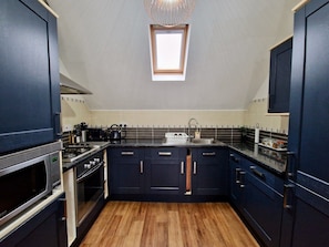 A compact kitchen with dark cabinetry, a built-in oven, a microwave, and a window above the sink. - Spacious, Chic & Modern Apt w/ Free Parking (Coventry)