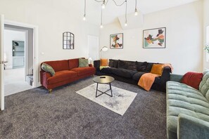 Un salon avec un canapé rouge, un canapé noir et un fauteuil vert. Une table basse se trouve au centre de la pièce.