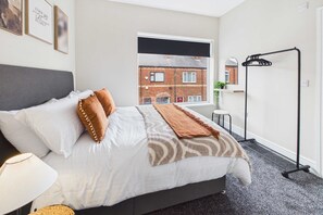 Une chambre à coucher avec un lit, une fenêtre, un miroir et un portant à vêtements noir.