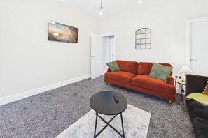 A living room with a sofa, a coffee table, a painting, and a mirror on the wall. - 4 Bed House with Garden - Perfect for Contractors and Families (Allerton Bywater)