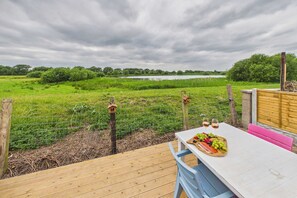 An outdoor dining area with a view of a lake and greenery, featuring a wooden deck, a table with a fruit platter, and a bench. - 4 Bed House with Garden - Perfect for Contractors and Families (Allerton Bywater)