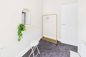 A bathroom with a white door, a mirror, a small stool, a plant on a shelf, and a gold-colored towel rack. - 4 Bed House with Garden - Perfect for Contractors and Families (Allerton Bywater)