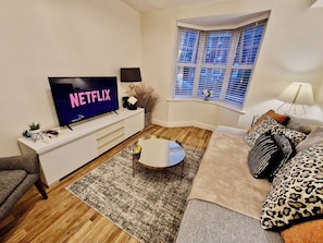 A modern living room with a flat-screen TV, a round coffee table, a sofa, and a window with blinds. - Spacious & Spacious Apt w/ Study | Free Parking (Coventry)