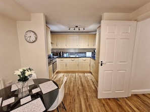 A kitchen with wooden cabinets, a dining table with placemats, and a clock on the wall. - Spacious & Spacious Apt w/ Study | Free Parking (Coventry)
