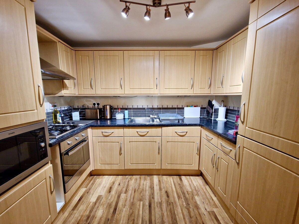 A kitchen with light wood cabinets, a black countertop, and stainless steel appliances.