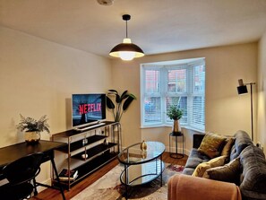 A modern living room with a flat-screen TV, a sofa, a coffee table, and a dining area with a glass-top table and chairs. - Stylish Apt in Trendy Earlsdon, Free Parking (Coventry)