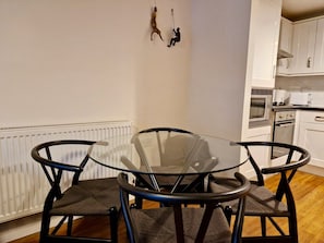 A dining area with a glass table and chairs, a white radiator, and a kitchen in the background. - Stylish Apt in Trendy Earlsdon, Free Parking (Coventry)
