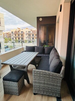 A balcony with a wooden table and wicker furniture, overlooking a residential area. - Apartment Valentino Golf Villamartin (Orihuela)