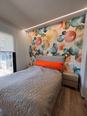 Een slaapkamer met een bed, een nachtkastje, een muur met een rond patroon en een raam.